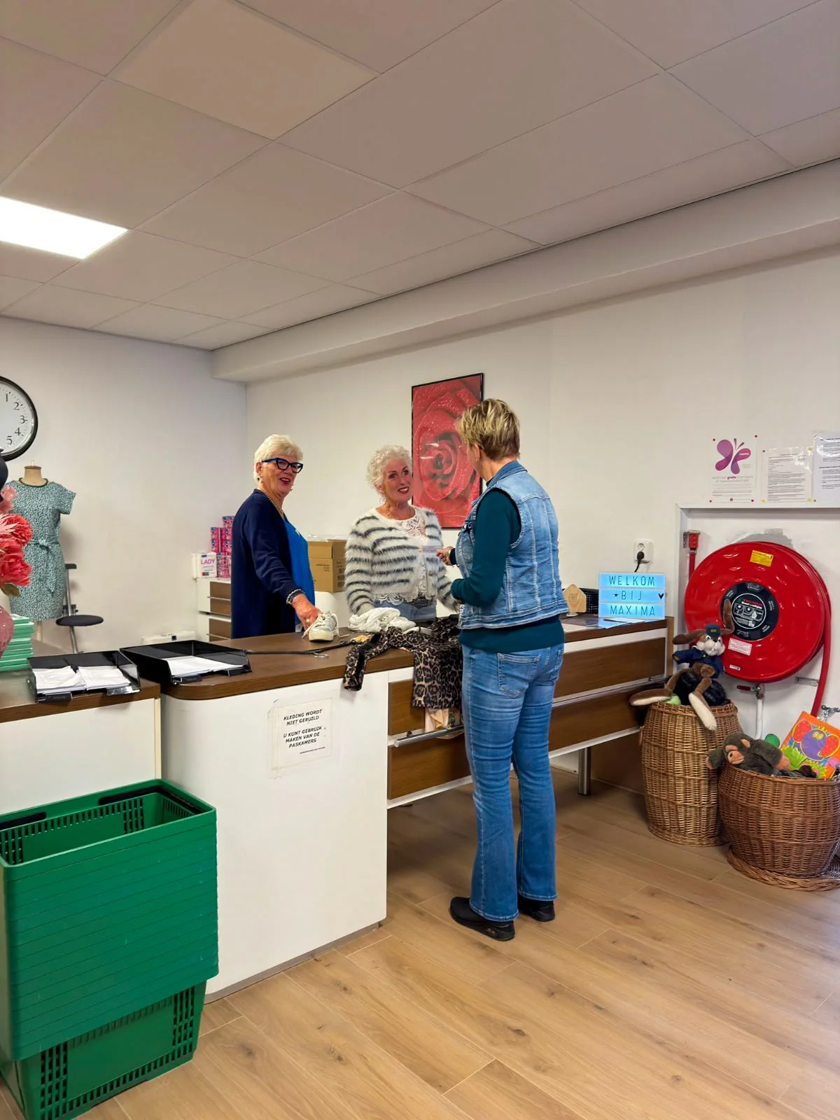 Vrijwilligers heten een bezoeker welkom bij de balie van Kledingbank Maxima in Sappemeer